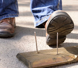 Worker with boots about to step on a big long sharp nail