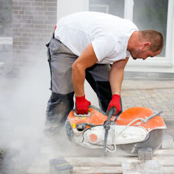 Worker without the proper PPE using a saw to cut cement surface.