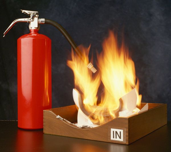 File bin with papers on fire on desktop with fire extinguisher nearby