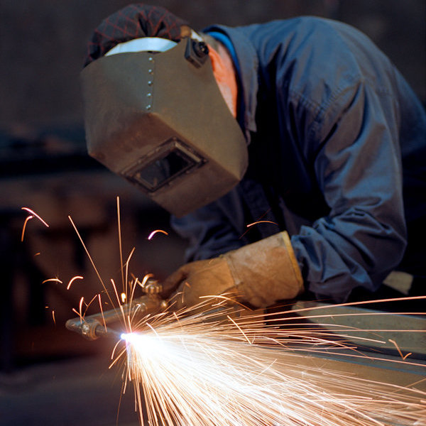 Worker with welding mask and other PPE welding with many sparks flying around.