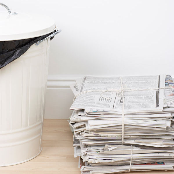 Newspapers stacked next to trash bin.