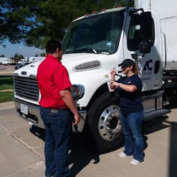 New driver receiving orientation from supervisor in front of large truck.