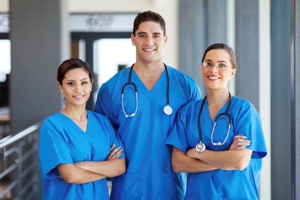 Three healthcare provided dressed in blue scrubs facing camera