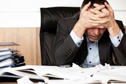 Image of manager sitting at desk hands over forehead overwhelmed by stress.