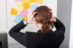 Image of worker under stress looking at notes on a wall and placing hands on her head.