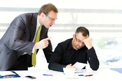 Image of manager yelling at worker sitting at his desk.