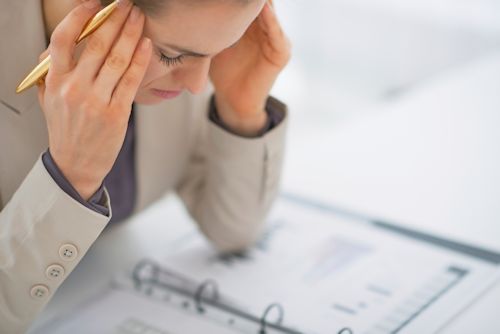 Image of employee elbows on desktop and head down showing signs of headache and stress.