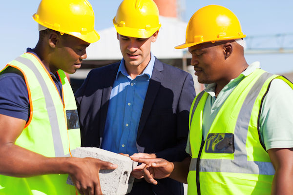 Three workers outside standing having a meeting and reviewing papers.