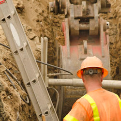 Worker on a ladder in a trench and an excavator.