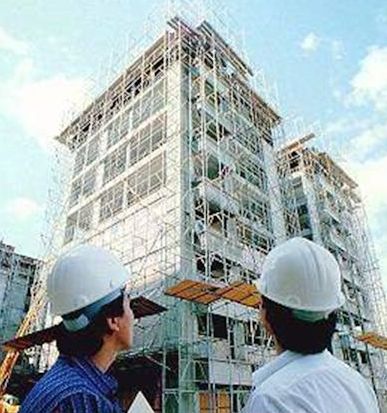 Two workers looking at scaffolding going up the side of a multi-story building