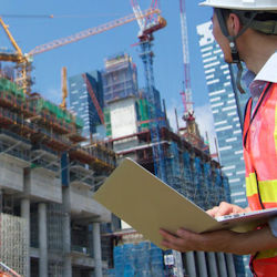 Worker with laptop outside looking up to complex group of cranes on a rooftop