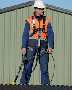 Worker wearing a fall restraint system while standing on top of a roof.