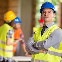 Competent and qualifer person in the foreground with two workers in the background; all have PPE on