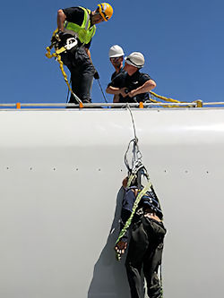 three workers on a roof performing a hands--on rescue of another worker