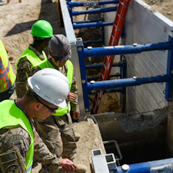 Three workers looking into trench