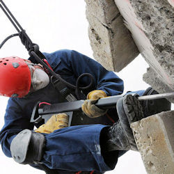 A worker using heavy tool while suspended in a very awkward position.