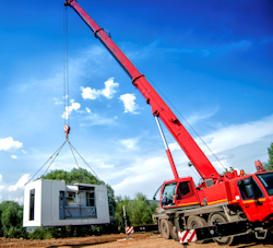 Crane lifting a portable office unit.