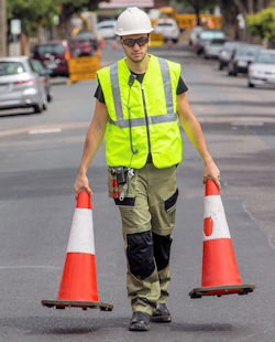 Worker picking up traffic cones in street.