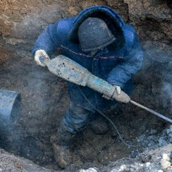 Worker using punch drill in trench