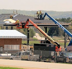 Two cranes working near one another delivering workers to a roof top