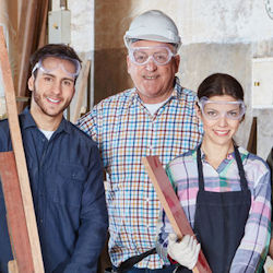 Three workers standing together holding building materials wearing PPE