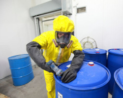 Completely protected by PPE this employee is opening drums with possible hazardous chemicals