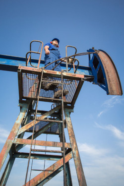 Worker standing atop a tall tower to analyze wellsite project for fall hazards