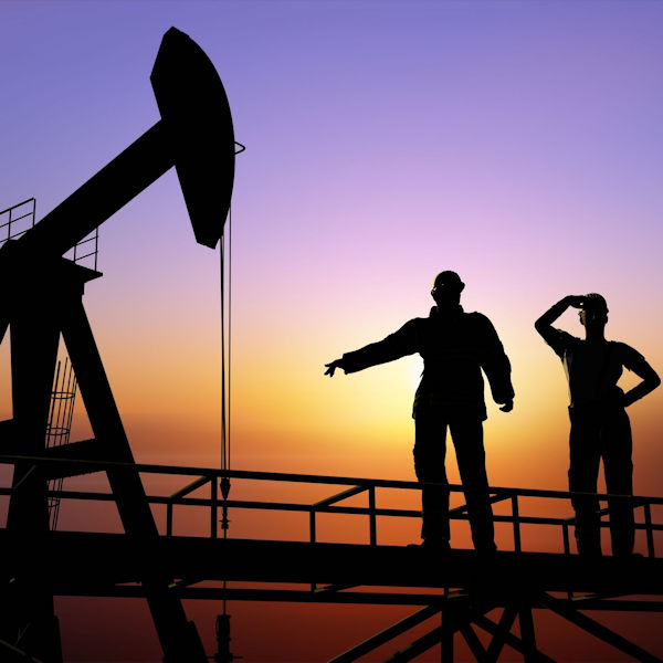 Two workers standing with sunset in background facing a oil pump