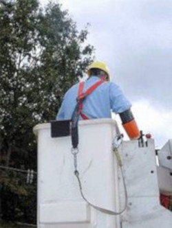 Man working ourdoors, wearing a harness and lanyard, in a manlift basket.