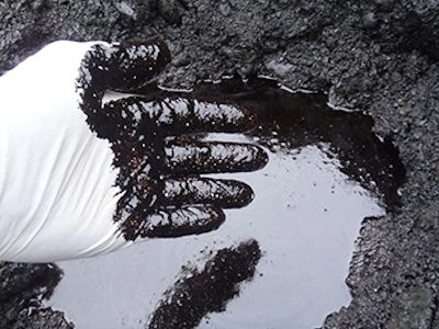 gloved hand reaching into a puddle of crude oil