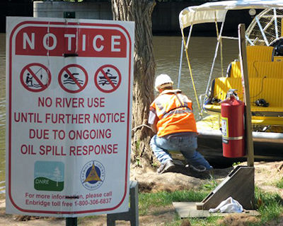 Warning sign by river that has been impacted by environmental damage of oil spill