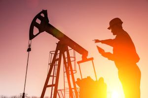 Image of engineer looking at laptop in front of oil well